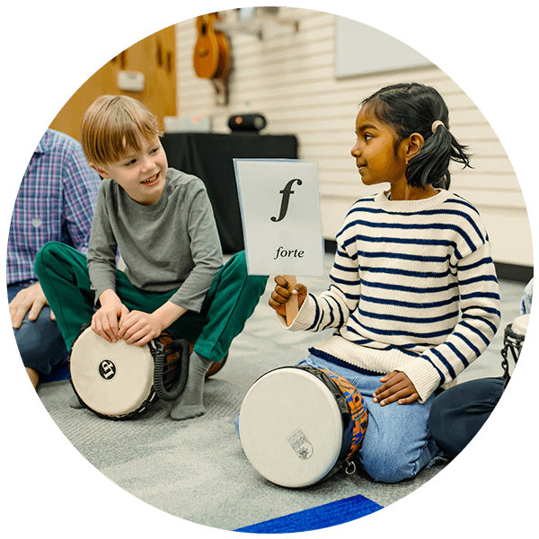 two children on floor with djembe drums under them and one child holding up a sign with a fortissimo indication on it