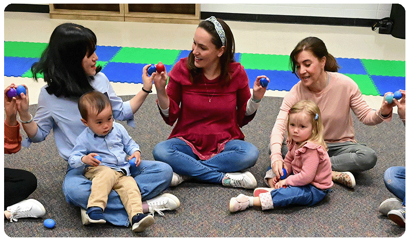 mothers holding egg shakers and singing with children in laps during a Music Together® class