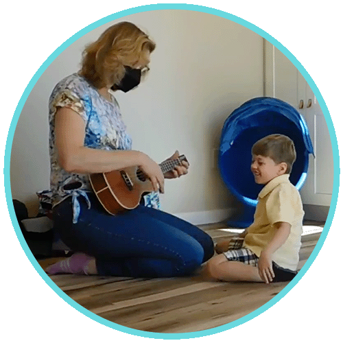 Max sitting on floor next to Music Therapist who is playing ukulele