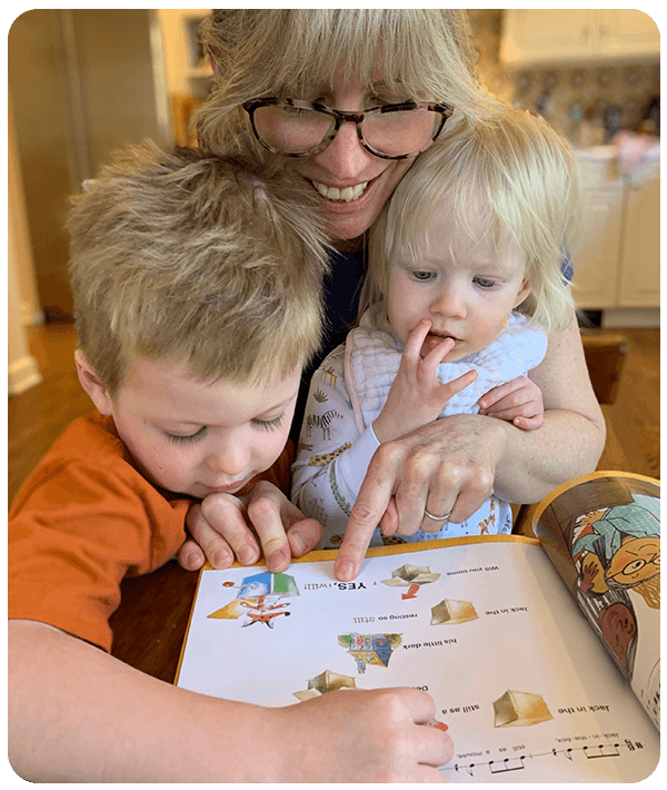 mom showing older child songbook with younger child in lap